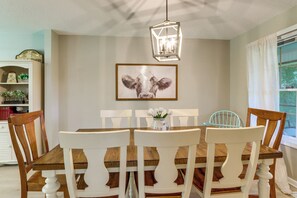 Een eetruimte met een houten tafel, witte stoelen en een hanglamp.