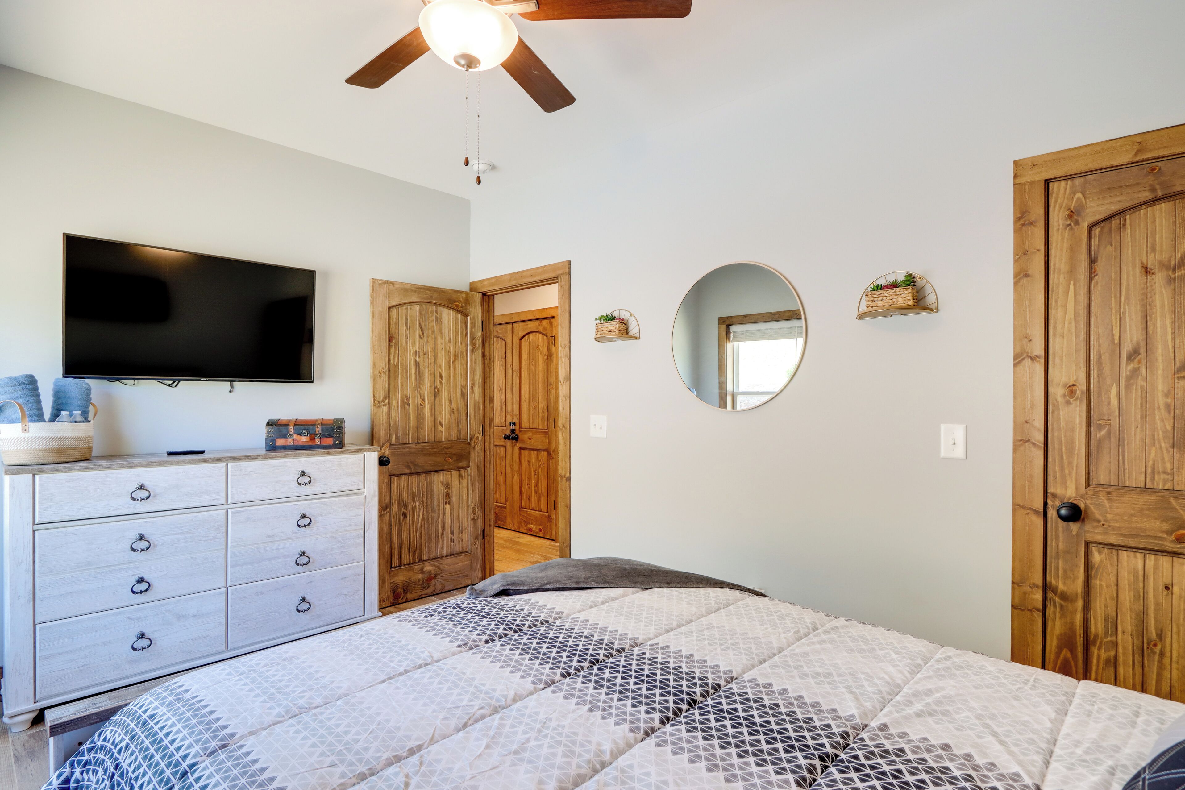 A bedroom with a bed, a dresser, a television, a ceiling fan, and wooden doors.