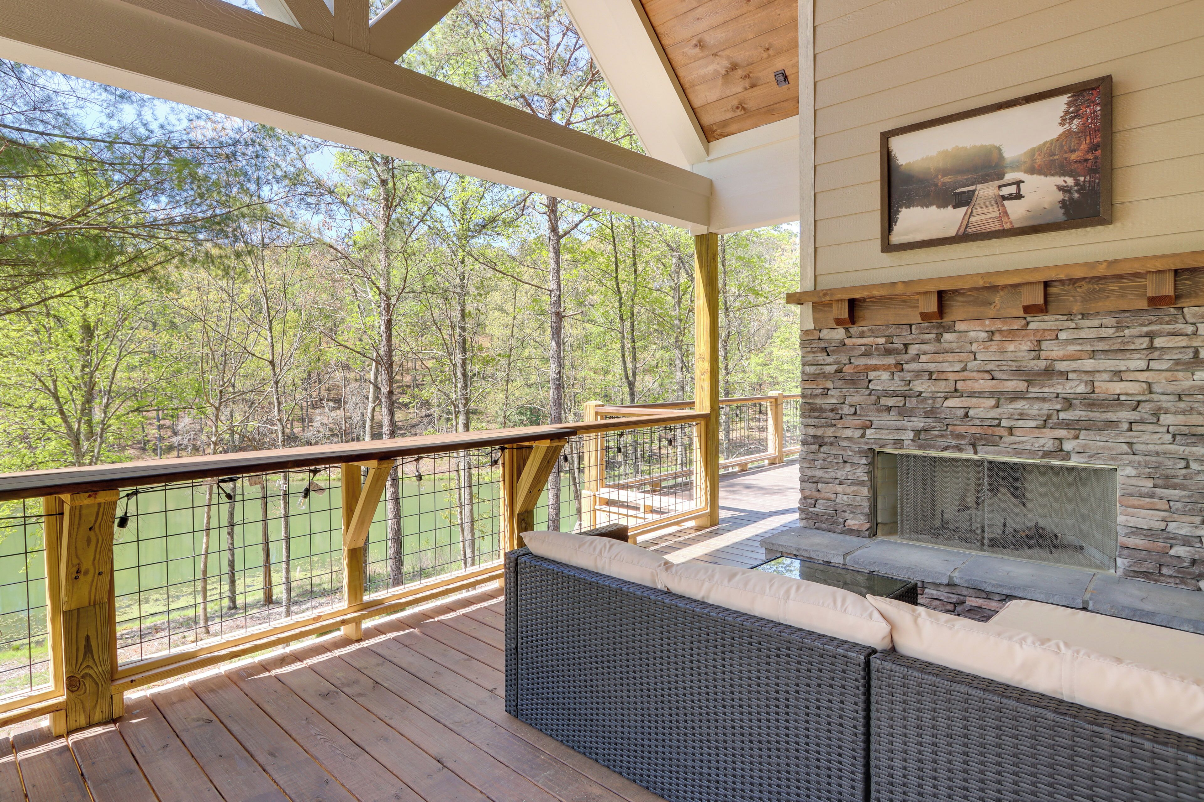 A covered deck with a stone fireplace, outdoor seating, and a view of a forested area.