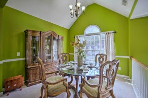 Een eetkamer met een glazen tafel, houten stoelen, een vitrinekast en een raam met gordijnen.