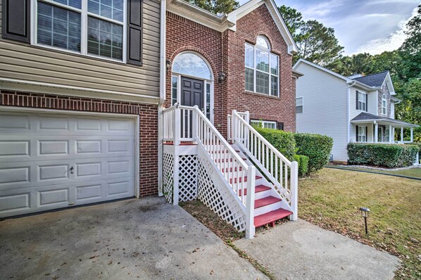 A two-story house with a front garage, a white staircase with a lattice balustrade, and a brick facade. - Spacious Acworth Home w/ Deck ~ 1 Mi to Lake (Acworth)