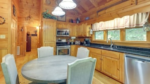 Ein Holzblock-Interieur mit Esstisch, Stühlen, Küchenzeile und großen Fenstern.