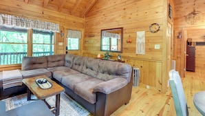 Ein Holzblockhaus-Interieur mit einer Eckcouch, einem kleinen Tisch und einem Fenster mit einem Karomustervorhang.