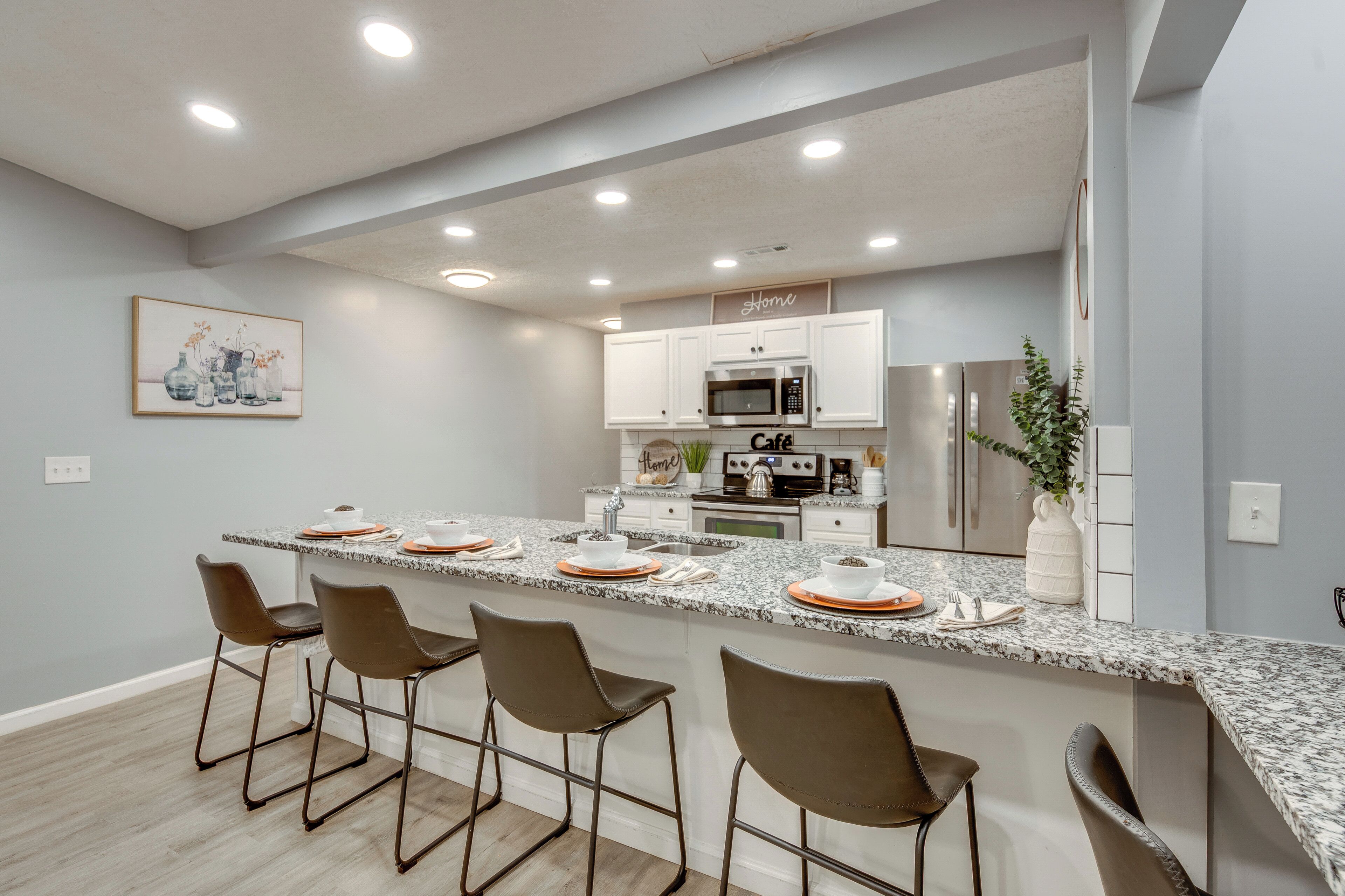 Una cocina moderna con una isla central, taburetes de bar, electrodomésticos de acero inoxidable y un elemento decorativo en la pared.
