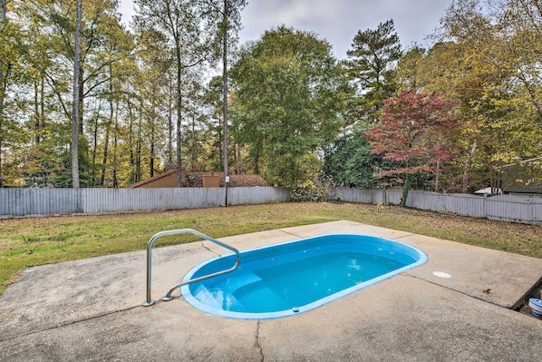 Un jardin avec une piscine, entouré d’arbres et délimité par une clôture en bois.