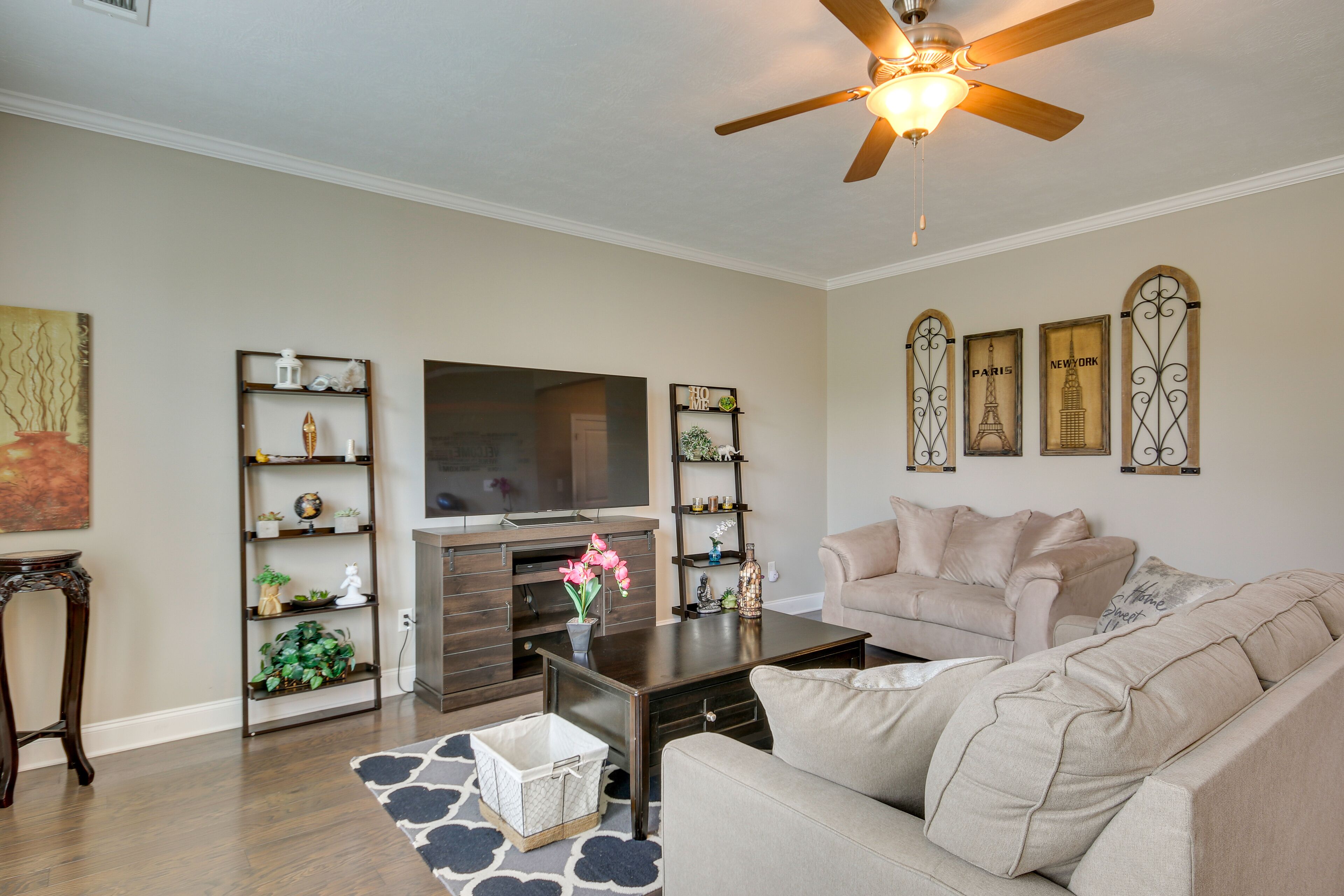 A living room with a beige sofa, a coffee table, a TV, and decorative shelves.
