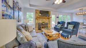 A spacious living room with a stone fireplace, comfortable seating, and a large TV. - Waterfront Sparta Home w/ Game Room & Fire Pit! (Eatonton)