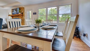 A dining area with a wooden table set for four, white chairs, and a stone fireplace. - Waterfront Sparta Home w/ Game Room & Fire Pit! (Eatonton)