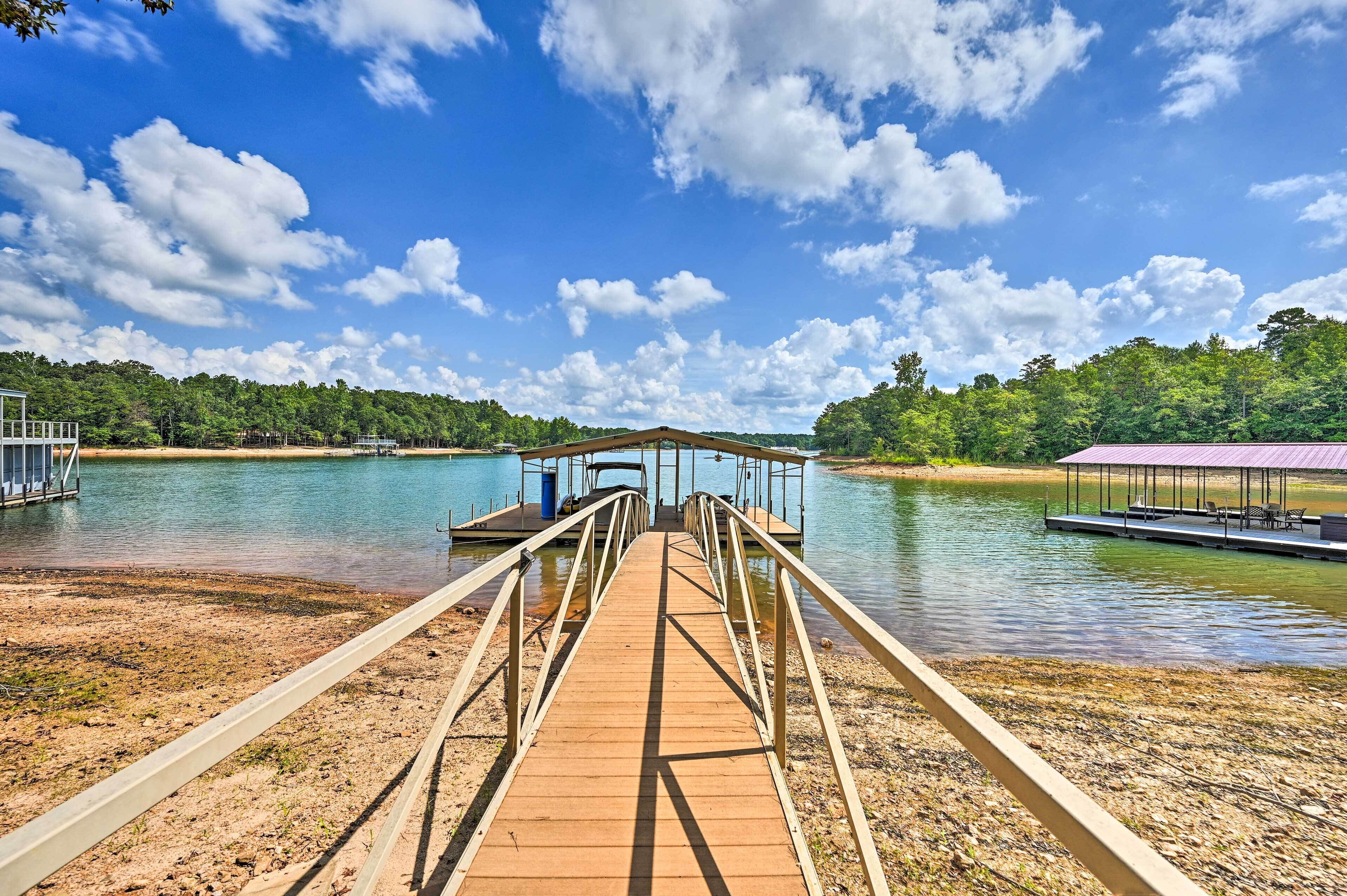 A wooden pier leading to a covered dock area with a view of a lake and forested hills.