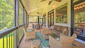 A covered outdoor area with wicker furniture, a ceiling fan, and large windows offering a view of the outdoors. - Upscale Family Home w/ Dock on Lake Hartwell! (Hartwell)