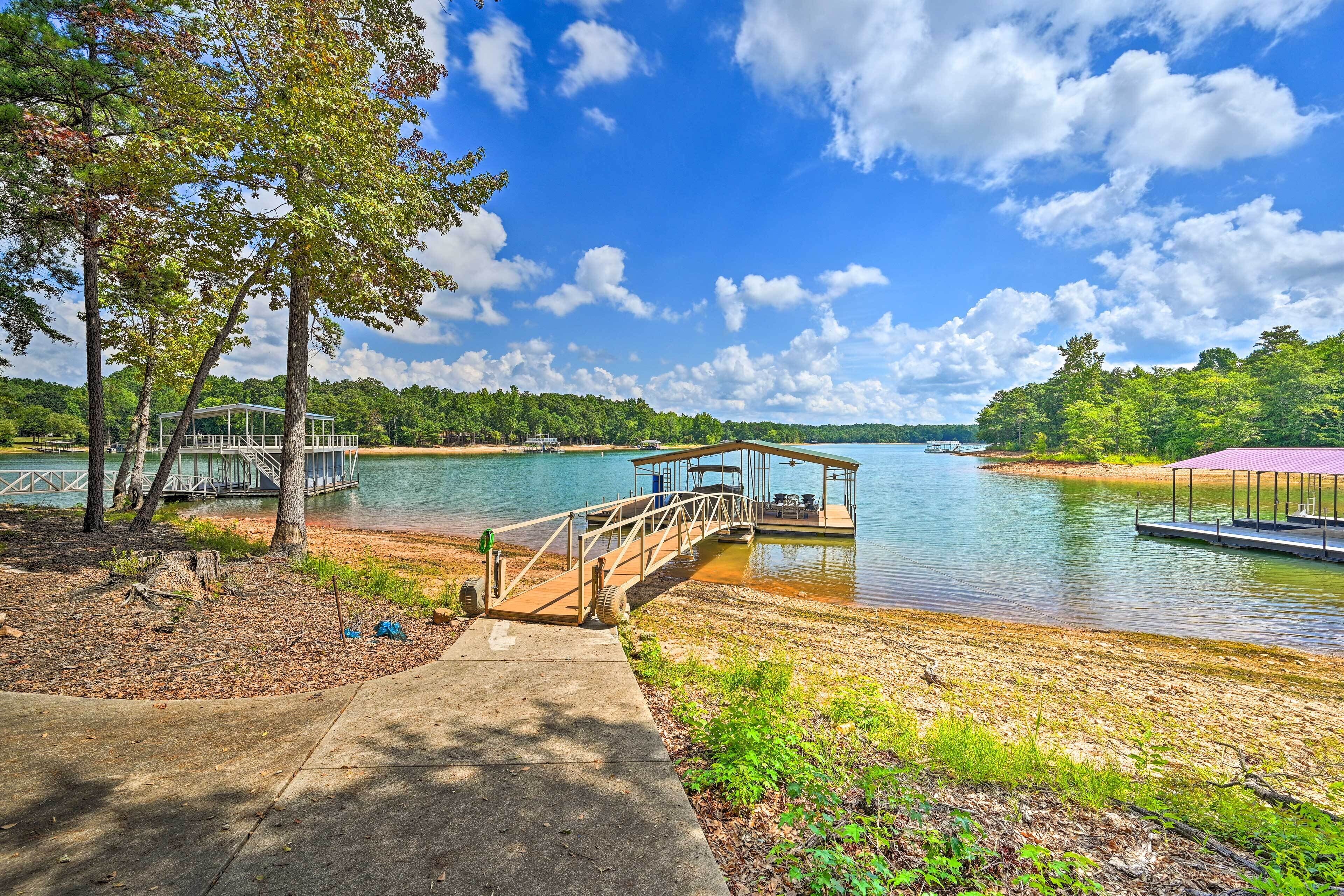 A lakeside park with a wooden bridge, a covered pavilion, and a dock.