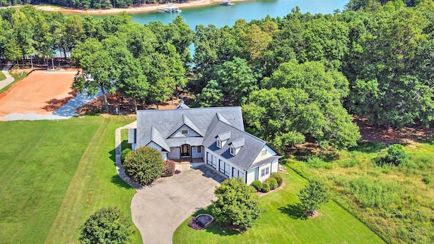 A large, two-story house with a spacious front yard, a driveway, and a view of a lake and forested area. - Upscale Family Home w/ Dock on Lake Hartwell! (Hartwell)