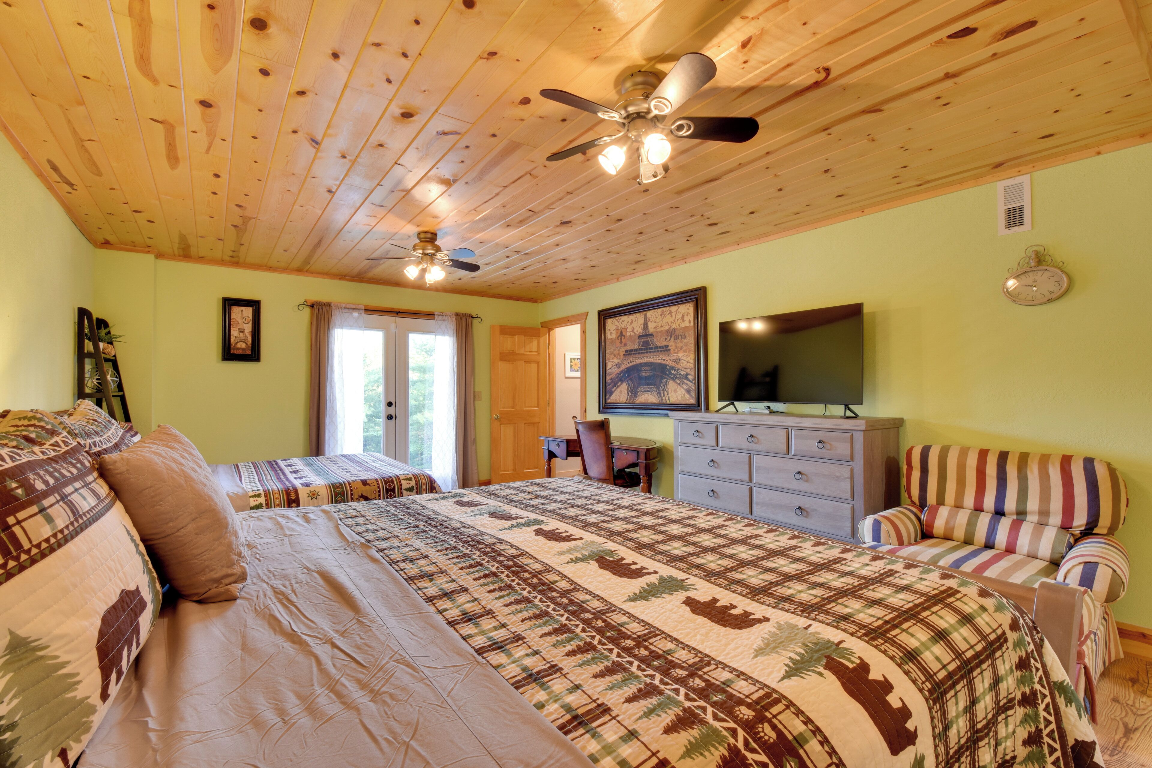 A bedroom with two beds, a ceiling fan, a dresser, a chair, and a painting on the wall.