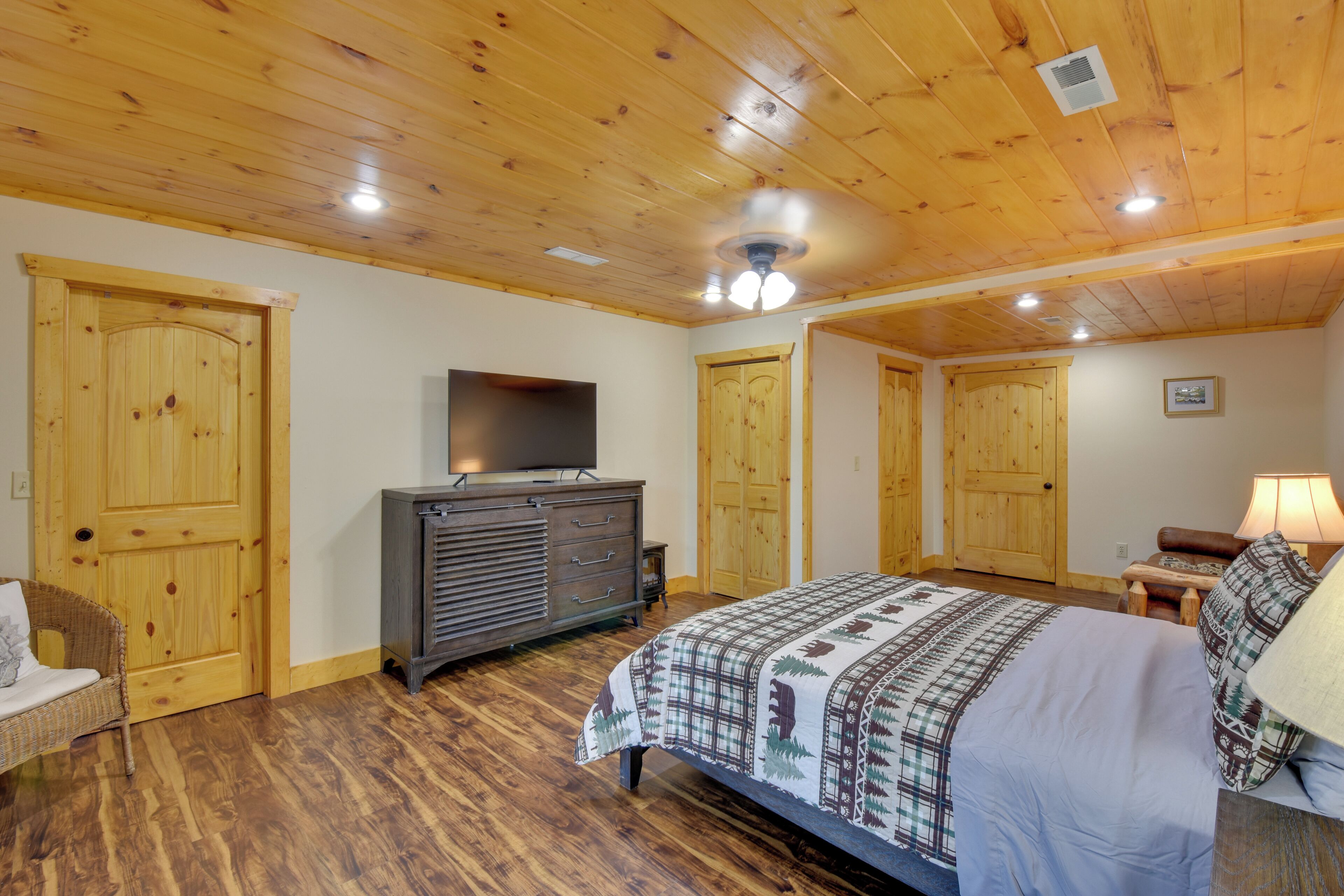 Een slaapkamer met houten vloeren, een bed met een bedsprei met dessin, een dressoir, een televisie op een standaard, en houten deuren.