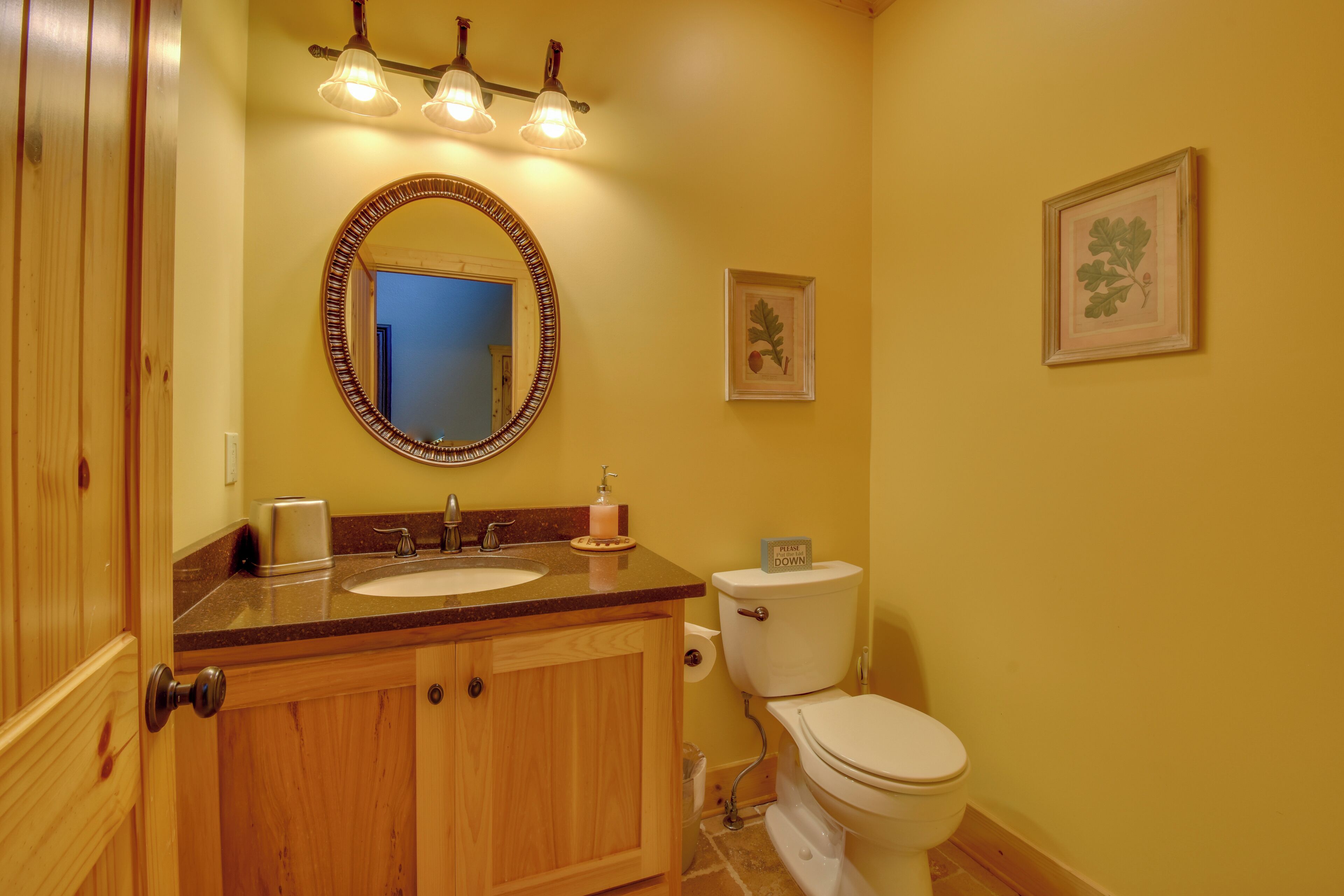 Un baño con armarios de madera, lavabo doble, inodoro y espejo con marco decorativo.