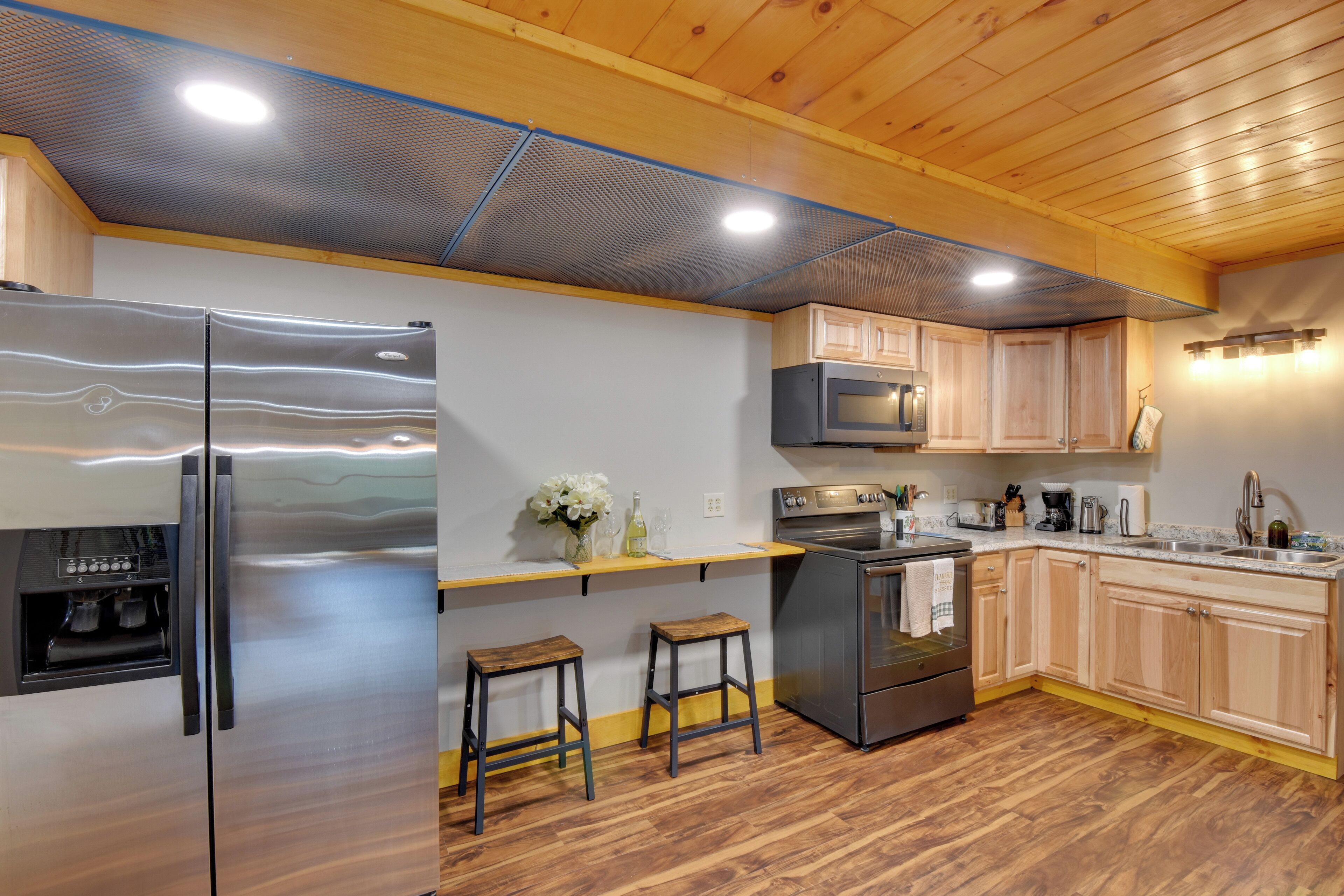 Una cucina moderna con elettrodomestici in acciaio inossidabile, sgabelli da bar in legno e soffitto in legno.