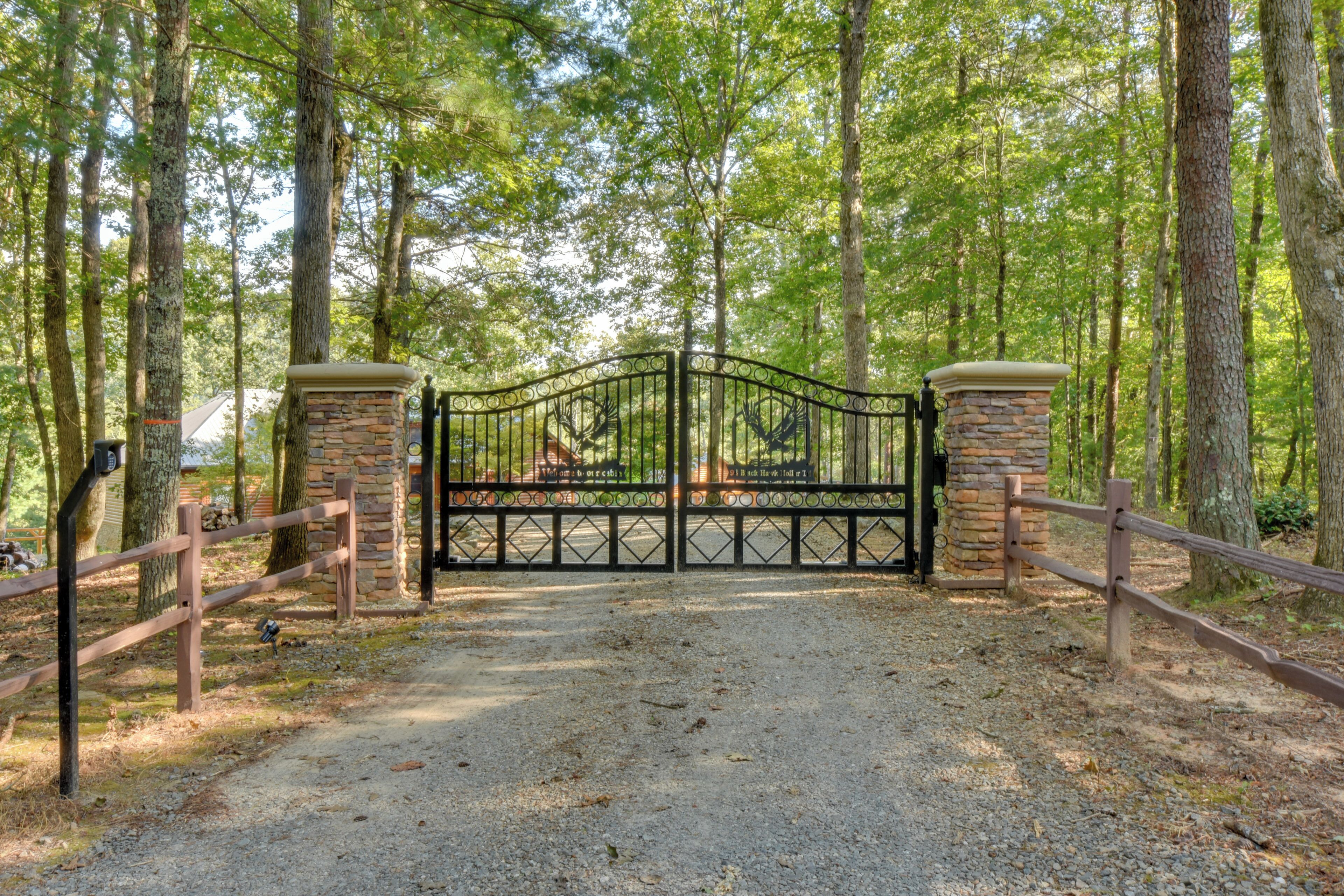 A gated entrance to a wooded area with a gravel path leading through.