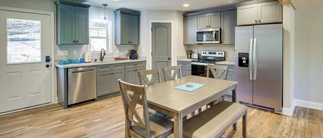A modern kitchen with grey cabinets, stainless steel appliances, and a wooden dining table with chairs.