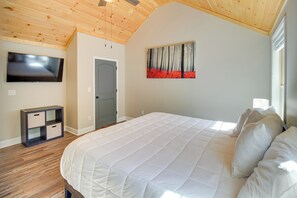A bedroom with a large bed, a television on the wall, and a painting above the bed. - Modern Ellijay Cabin Rental w/ Outdoor Fireplace (Ellijay)