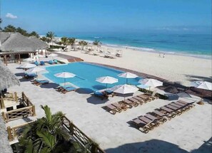 Relax by the pool or on the adjacent beach, surrounded by lounge chairs and umbrellas.