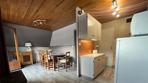 A compact kitchen with wooden cabinets, a dining area with a table and chairs, and a refrigerator.