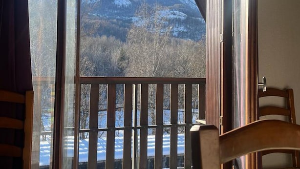 A room with a wooden chair and a view of a snowy mountain landscape through a large window.