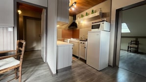 A compact kitchen with white cabinets, a microwave, and a refrigerator. There is a wooden ceiling and a window providing natural light.