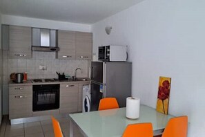 A modern kitchen with grey cabinets, a microwave, a refrigerator, and a dining area with orange chairs.