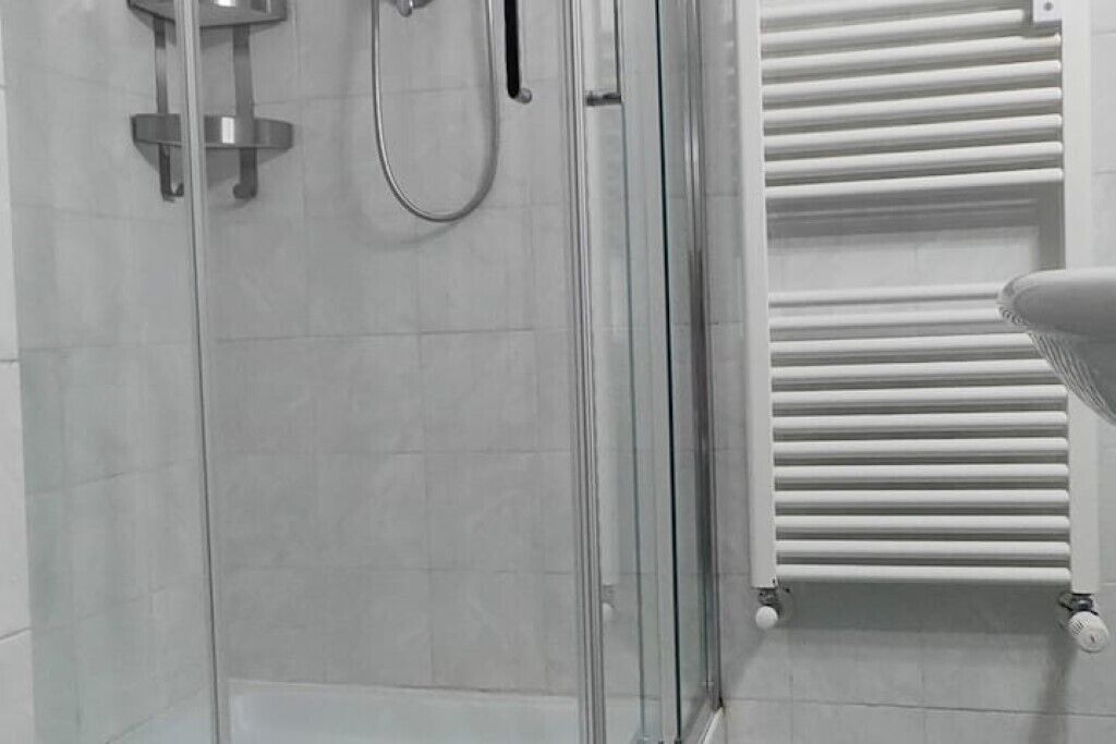A modern bathroom with a glass shower enclosure, a white radiator, and a towel rack.