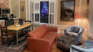 A living room with a brown leather sofa, a blue armchair, a dining table with a bowl of fruit, a kitchen area with a microwave, and a large window with a Christmas tree. -  Historic Waterfront District., for lovers of art, restaurants, unique shops, 

 (Warren)