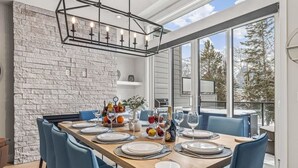 Un espace repas avec une longue table en bois, dressée pour six personnes, des chaises bleues et un mur en pierre en arrière-plan.
