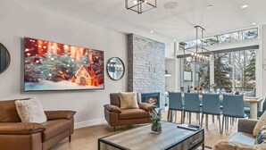 Un salon moderne avec une cheminée, un grand tableau et un coin repas offrant une vue sur les arbres.