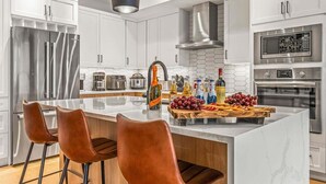 Une cuisine moderne avec des meubles blancs, des appareils en acier inoxydable et un îlot central doté de tabourets de bar.