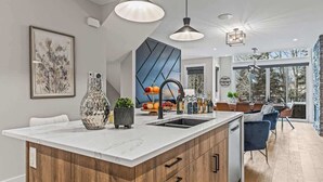 A modern kitchen with a marble countertop, wooden cabinetry, and pendant lighting. - NEW! Oberhofen by SSR Top View HOT TUB 5BR ( BL# RES-11737 ) (Canmore)