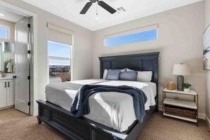 A bedroom with a large bed, a ceiling fan, a window, a nightstand, and a view of the outside.