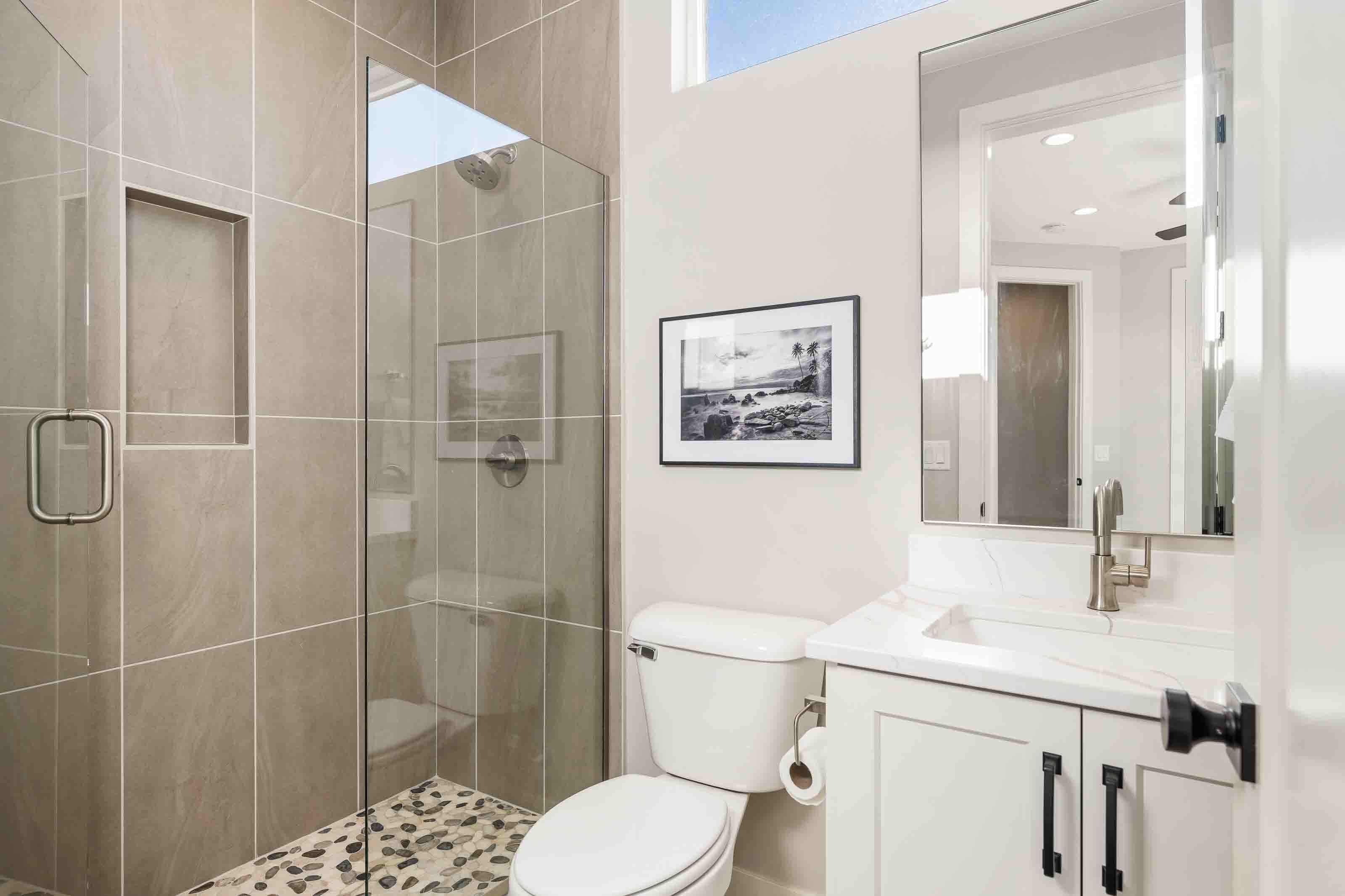 A modern bathroom with a glass shower enclosure, a toilet, and a sink with a mirror above it.