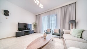 Een moderne woonkamer met een flatscreen-tv, een houten salontafel, een bank en een groot raam met gordijnen.