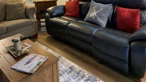 Una sala de estar con un sofá de cuero negro, una mesa de centro de madera y un ventanal con vista a árboles.