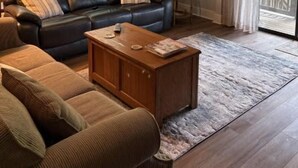 Una sala de estar acogedora con un sofá de cuero negro, una mesa de centro de madera y un ventilador de techo.