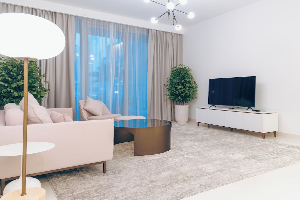Un salon moderne avec un canapé, une table basse, un téléviseur et de grandes fenêtres dotées de rideaux.