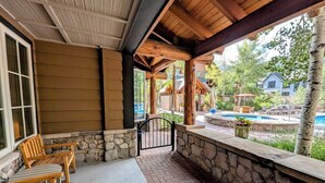 A covered patio area with wooden benches and a stone wall, leading to a pool area with a view of surrounding buildings. - River Run Summer Fun | Patio, Pool  & Hot Tub (Keystone)