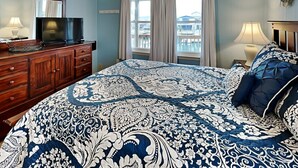 A bedroom with a large bed, a dresser, a television, and a window with curtains.