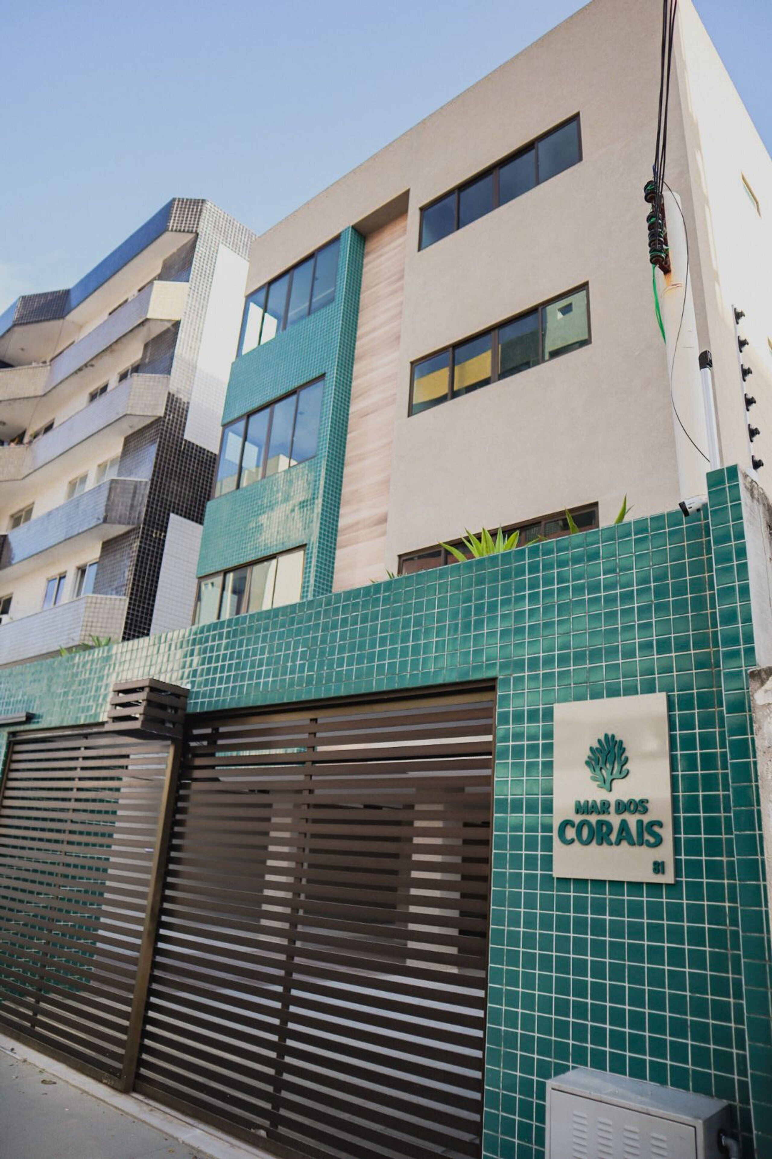 Un bâtiment à la façade recouverte de carreaux, une enseigne indiquant « MAR DOS CORAIS » et une entrée fermée par un portail.
