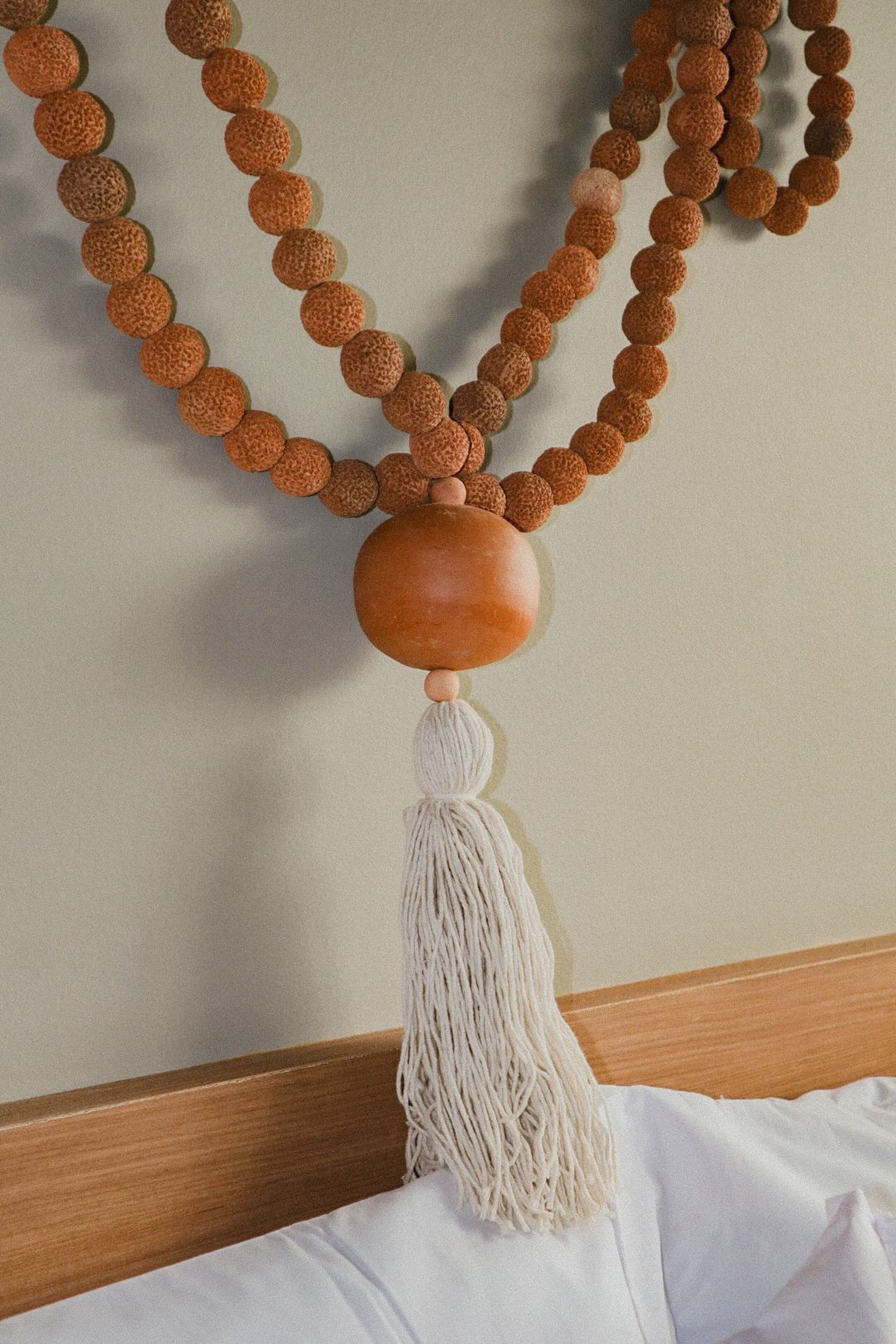 A bed with a wooden headboard and a macramé wall hanging with a tassel.