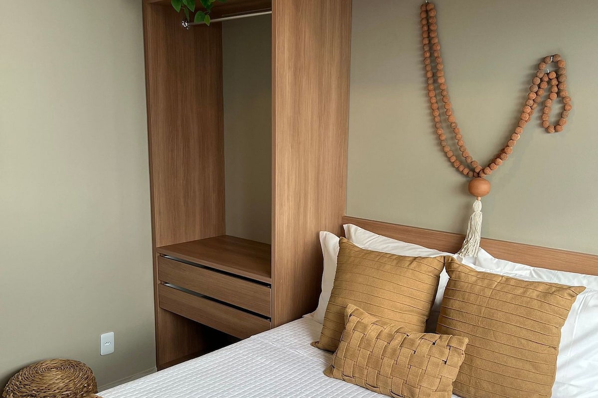 Ein Schlafzimmer mit einem Bett, einem Holzschrank, einer hängenden Pflanze und einer Gebetsreih gestreiften Halskette an der Wand.