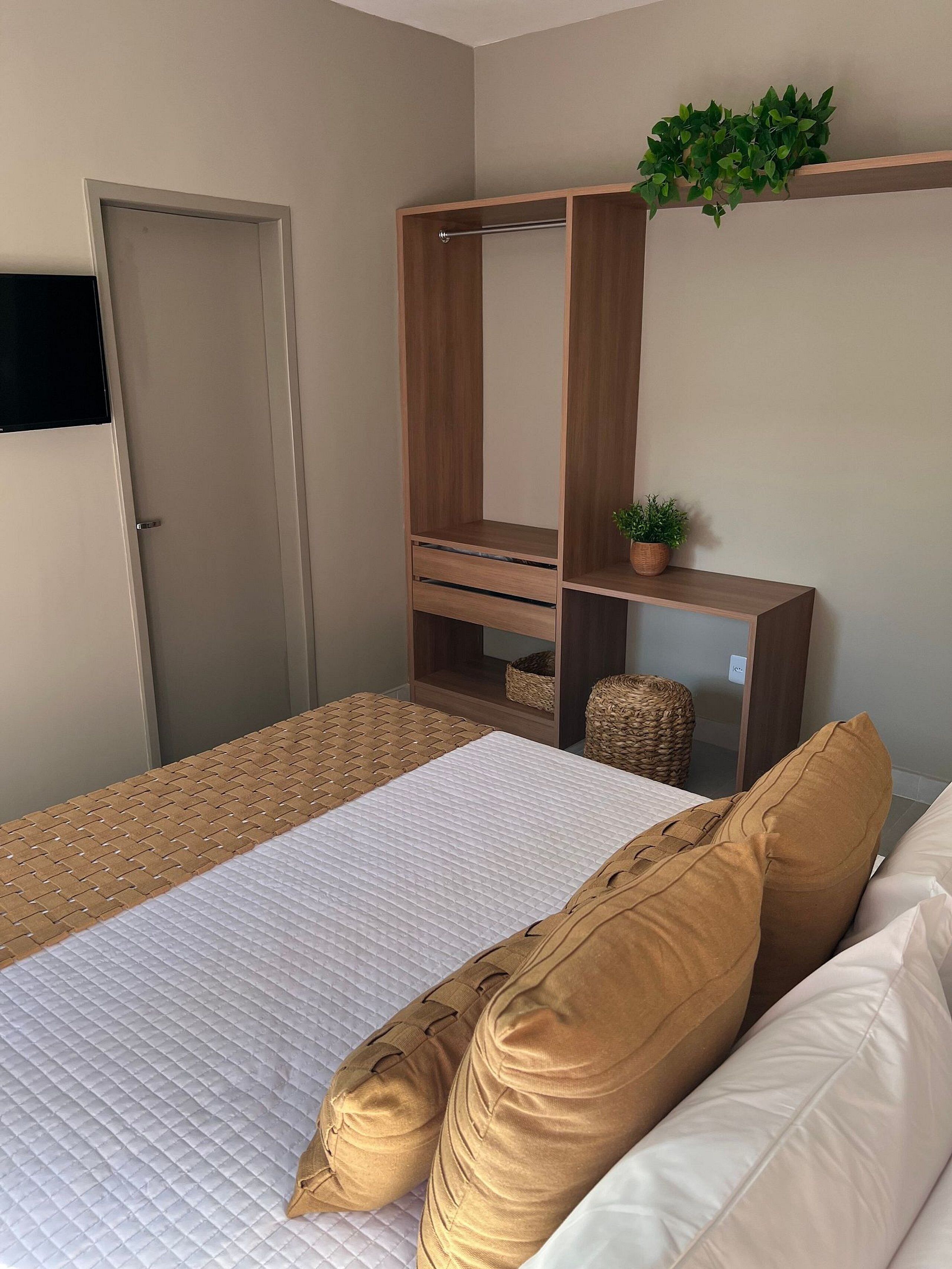 A bedroom with a bed, wooden wardrobe, a small plant, and a television on the wall.