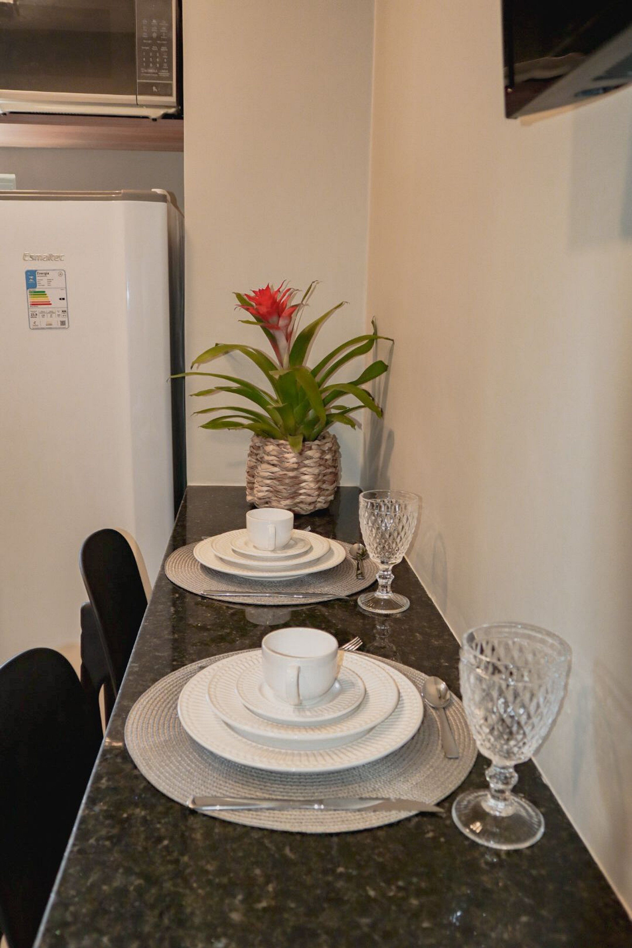 A dining area with a granite table, white plates, cutlery, and a potted plant.
