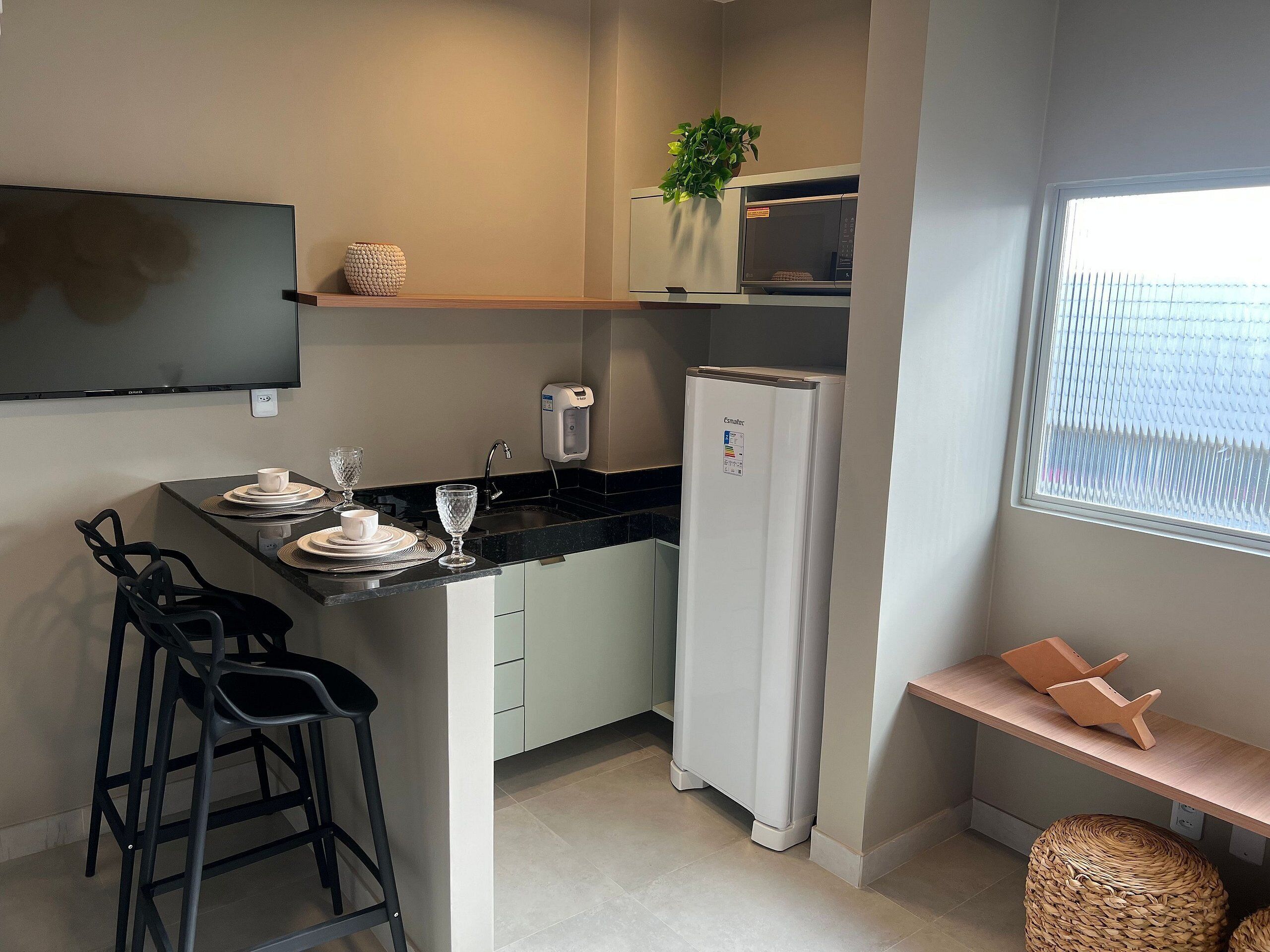 Eine kompakte Küche mit Kühlschrank, Mikrowelle und einer kleinen Essecke mit Hocker.