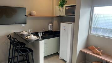 Eine kompakte Küche mit Kühlschrank, Mikrowelle und einer kleinen Essecke mit Hocker.