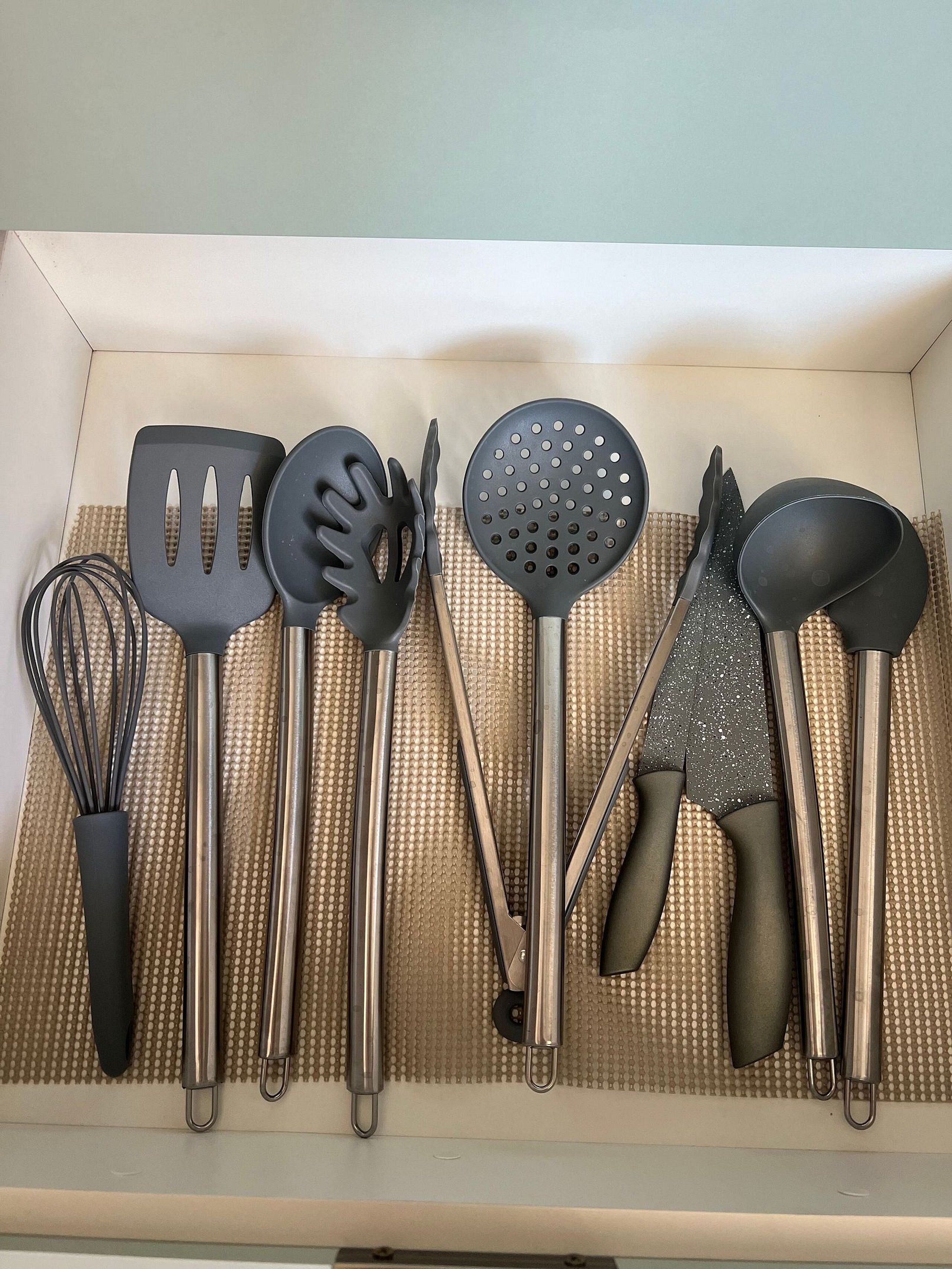A kitchen drawer with various utensils including a whisk, spatulas, and a grater.